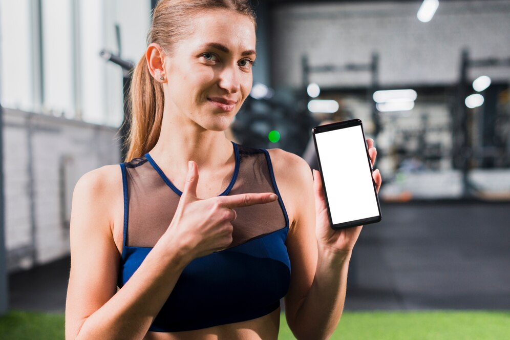 A satisfied fitness woman recommending a studio management software pointing at her phone. Source: Freepik